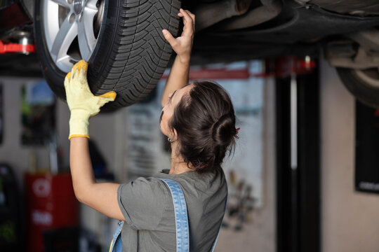 A woman skillfully holds a tire while working on a vehicle in a garage setting, showcasing determination and expertise.