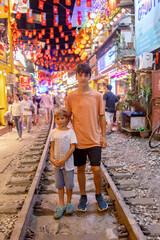 Train street in Hanoi in the evening. Child posing on the railway in Hanoi, train passing very close to the cafe shops