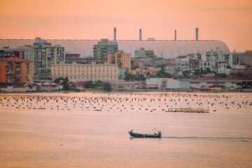 Wide coastal view of Taranto with boats, city skyline and glowing orange horizon