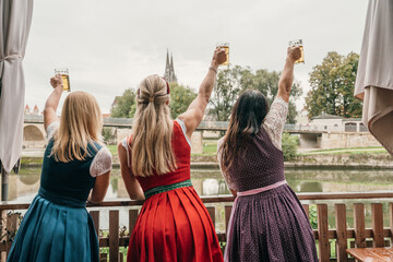 Fototapeta premium Women in colorful dirndl dresses enjoy Bavarian tradition in a beer garden near the Danube in Regensburg Germany