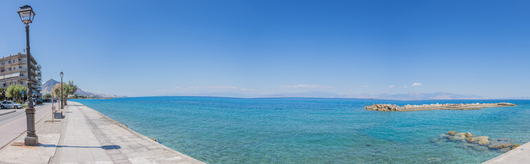 Obraz premium Blue, calm mediterranean sea at the promenade of Xylocastro, gulf of Corinth, Peloponnes, Greece (panorama)