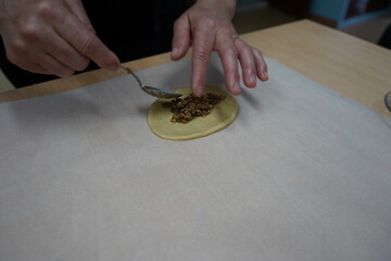 A person is spooning a traditional Cretan filling of walnuts, black and golden raisins and cinnamon onto a piece of dough, preparing it to be shaped into a Lazaraki symbolizing the resurrection.