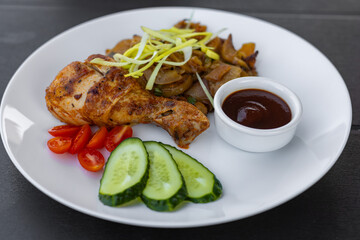 white plate with potatoes and onions, garnished with fresh leek. Side of sweet cherry tomato halves, cucumber slices and rich barbecue sauce 