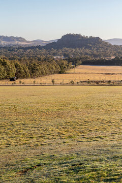 Vertical view of Hanging Rock, a volcanic rock formation, in the Macedon Ranges, Victoria, Australia, with golden farmland and winter frost in soft morning light.