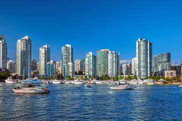 Obraz premium View of Vancouver Harbor and downtown Vancouver. A beautiful sunny day, blue water of the bay. Many boats and yachts on the foreshore, a row of skyscrapers and a blue sky
