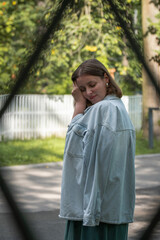 Portrait of a woman in a light denim jacket standing outdoors near a white wooden fence, looking over her shoulder thoughtfully