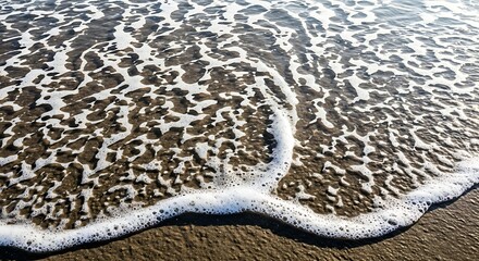 Obraz premium Foamy ocean water washing up on a sandy beach, close-up view.