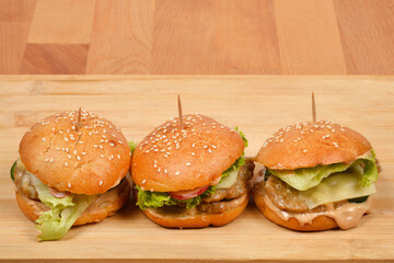 A horizontal shot of three homemade burgers with sesame buns, skewered with toothpicks and resting on a rustic wooden board