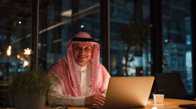 Happy Middle Eastern businessman working late in the evening in a modern glass office
