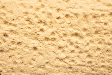 Textured surface of a yellow wall with uneven patterns and subtle imperfections, creating a warm and inviting atmosphere for interior design projects and artistic backgrounds