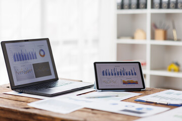 graphs charts, workspace, Laptop Computer, notebook, and eyeglasses sitting on a desk in a large open plan office space after working hours	

