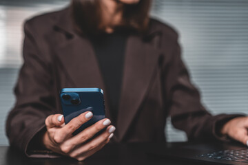 Businesswoman using smartphone and laptop at desk in modern offi
