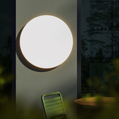 Glowing circular wall lamp on textured exterior wall at night with green chair and wooden table in foreground, modern lighting concept mockup scene. 3D Rendering
