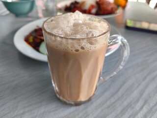 Traditional Malaysian Teh Tarik or pulled tea served in a glass with rich foam, popular hot milk tea drink in Southeast Asia and street food culture.