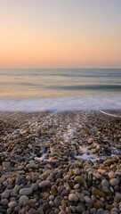 Calm ocean waves washing onto a rocky beach at sunset with pastel colored sky above