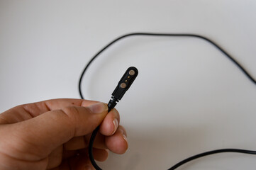 Hand holding a magnetic USB charging cable with connector pins, placed on a white background. Concept for electronics, device charging, and modern gadgets.