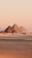 Three pyramids stand majestically in a vast, sandy desert under a pale, pinkish sky at sunset or sunrise, the closest pyramid is slightly smaller than the other two
