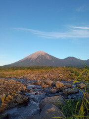 Long exposure of a rocky river below Mount Semeru at sunrise, highlighting the contrast of silky waters and textured volcanic mountain surfaces.