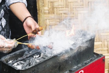 Grilling satay on charcoal with smoke and flames