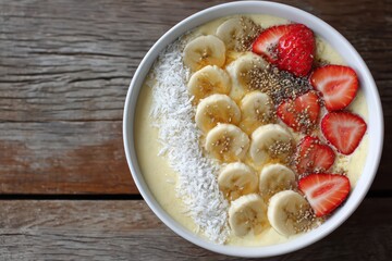 Healthy breakfast bowl with bananas, strawberries, chia seeds, and shredded coconut on a rustic wooden table for a nutritious start to the day