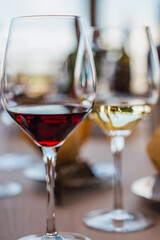 A detailed close-up shot of two elegant wine glasses, one filled with rich red wine and the other with crisp white wine, suggesting a wine tasting event. Bottles are blurred in the background.