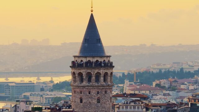 Istanbul, Turkey - May 12, 2025: Close up aerial view of the historic Galata Tower with tourists on the observation deck, with Istanbul's rooftops and Golden Horn in the background at sunrise