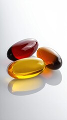 Three translucent capsules, amber, reddish-brown, and gold, rest on a reflective white surface, showcasing their oily contents and glossy shells