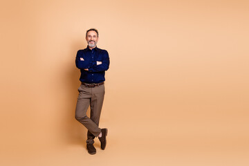 Confident mature businessman standing on beige background in formal attire with crossed arms and professional pose