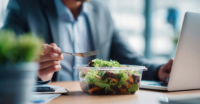 Office worker enjoys healthy salad while working on laptop during lunchtime in a modern workspace