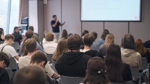 Group of individuals attentively listening to a presenter at a seminar in a modern venue.