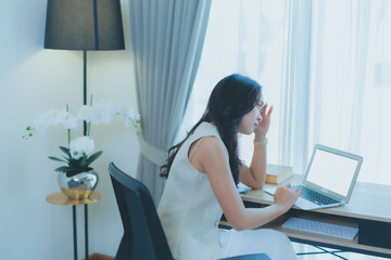 Asian woman feeling tired and stressed while working on her laptop from home, experiencing burnout...