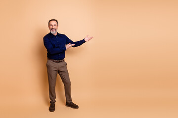 Confident senior businessman presenting with open arms against a beige studio background, showcasing professional elegance