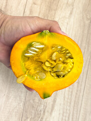 Hand holding fresh Hokkaido pumpkin slice with seeds, bright orange squash ready for cooking soups, stews or roasting, healthy seasonal ingredient closeup.