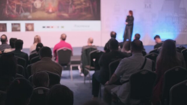 Audience members attending a speaker presentation showing slides in a professional conference setting.