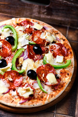 Pizza with chorizo ​​sausage, mozzarella cheese, green pepper and black olives. Rustic wooden background. Soft focus.	