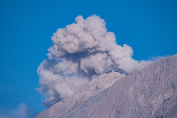 Close up view of Mount Semeru’s summit spewing smoke and volcanic ash under a bright blue sky, showcasing the natural beauty and rugged details of this powerful Indonesian volcano.