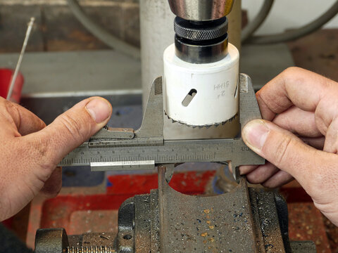 Closeup of machinist worker hands taking a diameter measurement of hole cut in a metal piece using calliper