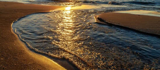 Sunlit water flows gently onto a sandy beach at golden hour