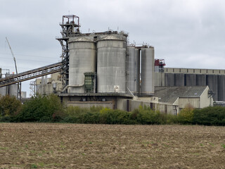 Obraz premium A large industrial factory with storage silos, located in a rural landscape next to a plowed agricultural field