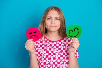 Young girl holding colorful happy and sad emotion symbols on a blue background wearing a checkered stylish t-shirt