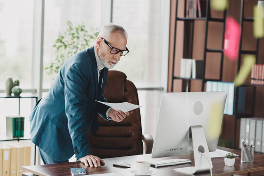 Senior businessman analyzing documents at his desk in a modern office workspace surrounded by professional tools and decor