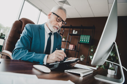 Confident senior businessman working on documents at desk in professional office environment while reviewing papers