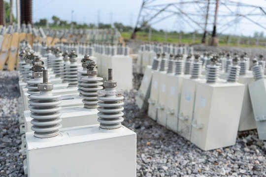 Close up of capacitor bank units with ceramic insulators at high voltage electrical substation, equipment for reactive power support, energy storage, and reliable electricity supply.