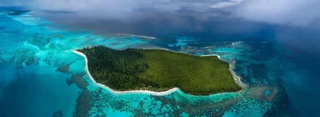 A stunning high-altitude aerial view of the remote Ilot Brosse, off the coast of the Isle of Pines. This untouched paradise is surrounded by a vibrant turquoise coral reef system