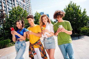 Group of cheerful friends using smartphones outdoors in a sunny park setting, enjoying leisure moments and bonding