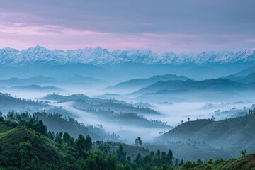 Misty dawn reveals a vast, layered mountain range, snow-capped peaks contrasting with the blue-hued valleys below, a tranquil, atmospheric scene