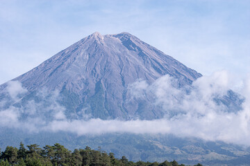 Mount Semeru’s iconic peak stands proudly against the expansive blue sky, its detailed volcanic ridges and textures clearly illuminated by daylight.
