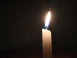 Minimalist image of a single white candle burning in a dark room. Soft warm glow symbolises hope, silence, solitude, or remembrance.