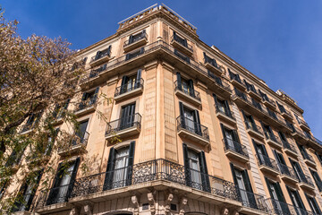 A majestic Barcelona tower block, adorned with intricate Art Nouveau architecture and windows. It stands majestically against the backdrop of a cloudy sky in its residential neighborhood.
