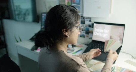 young woman working on laptop with color samples and paint shade cards spread on table, Interior designer at work with Paint swatches palette in hand for interior design project - Powered by Adobe